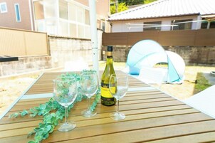 Une table en bois avec une bouteille et des verres, une tente et une clôture, le tout installé dans un jardin.