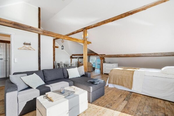 Un dormitorio estilo loft acogedor, con vigas de madera a la vista, un sofá gris, una cama blanca y piso de madera.