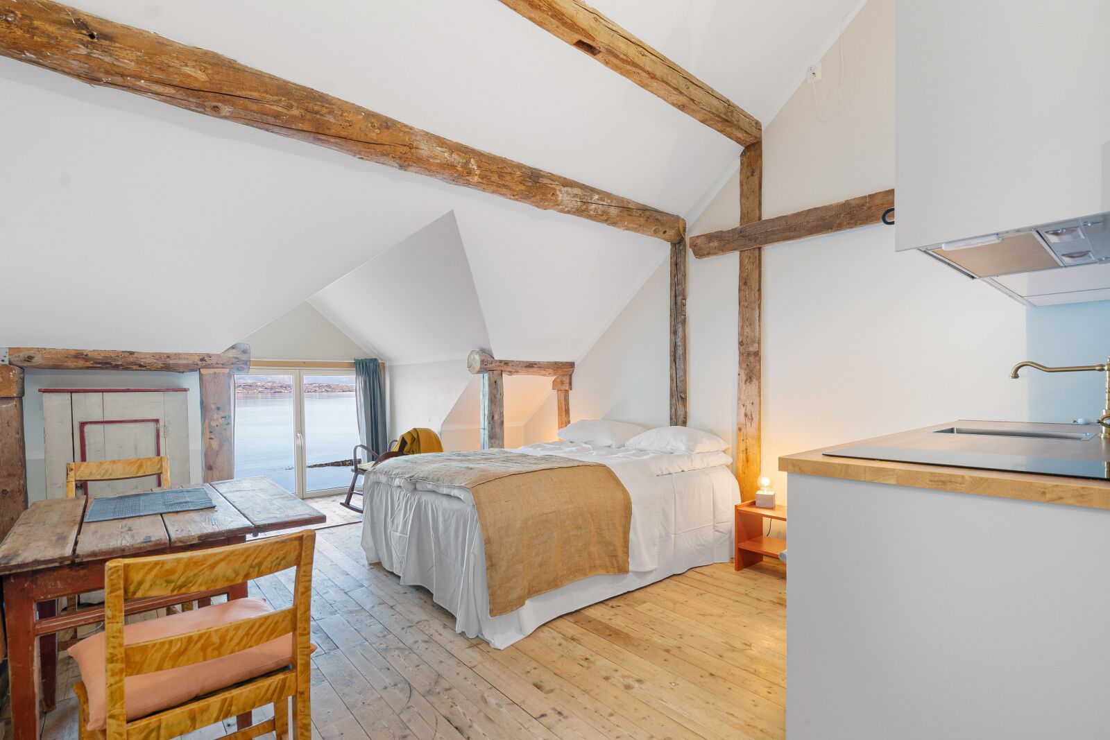 Un dormitorio acogedor en el ático con cama, vigas de madera, un escritorio y vistas al exterior.