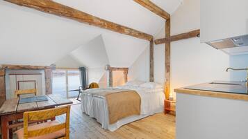 Un dormitorio acogedor en el ático con cama, vigas de madera, un escritorio y vistas al exterior.