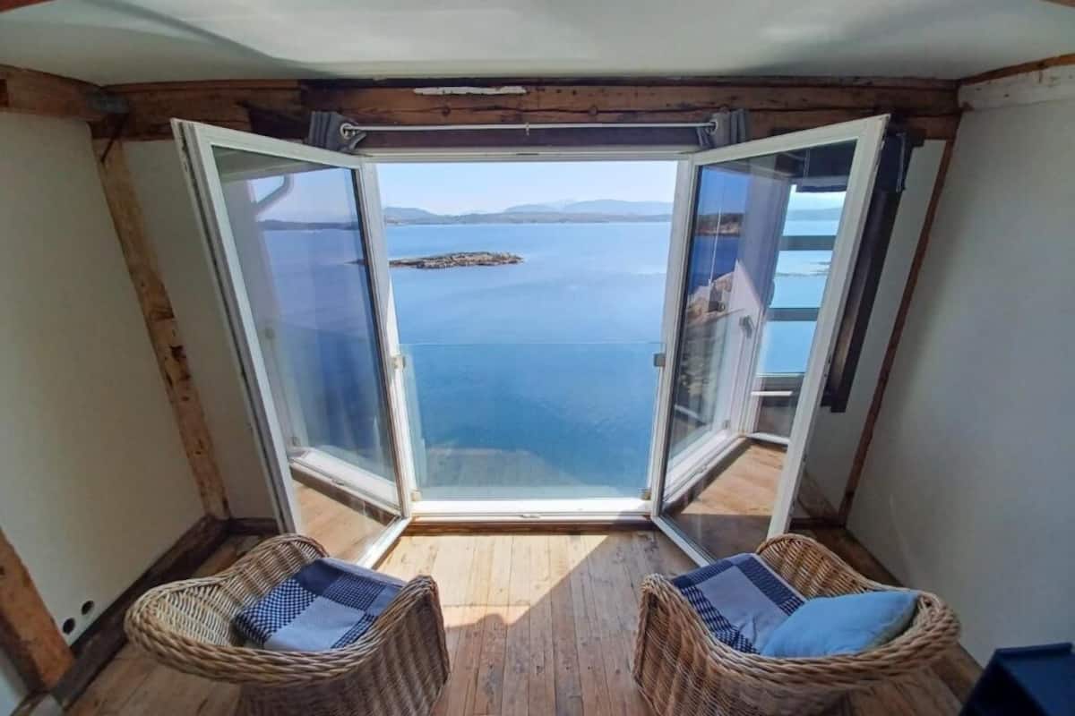 A balcony with wicker chairs and a glass door leading to a sea view.