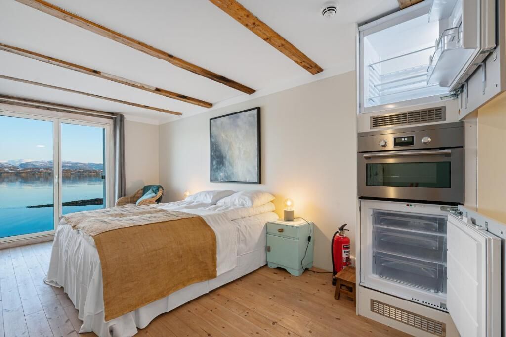 A bedroom with a bed, a nightstand, a window with a view of a body of water, and a built-in oven.