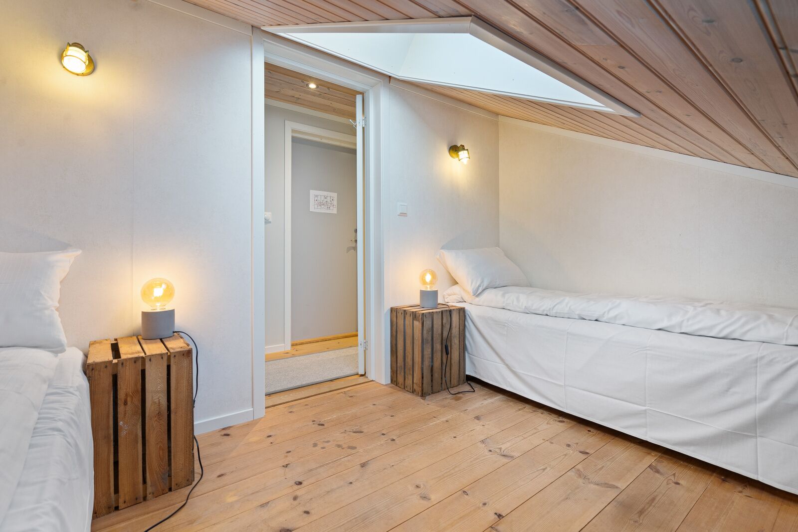 A cozy bedroom with two beds, wooden flooring, and a skylight.