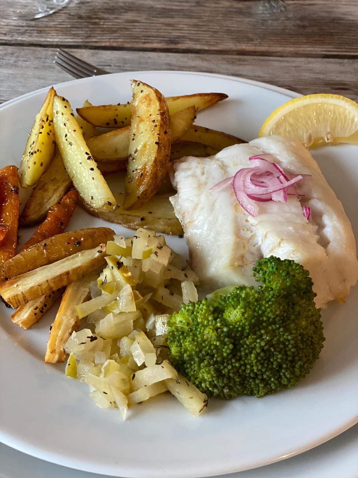Um prato com peixe, batatas, cebolas e brócolis.