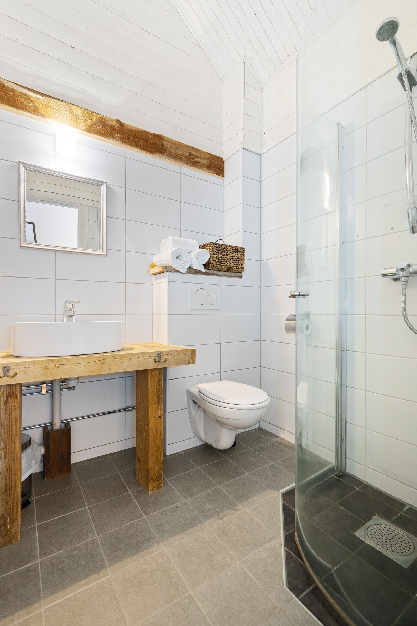 A bathroom with a wooden vanity, a white toilet, a glass shower enclosure, and a towel rack with folded towels.