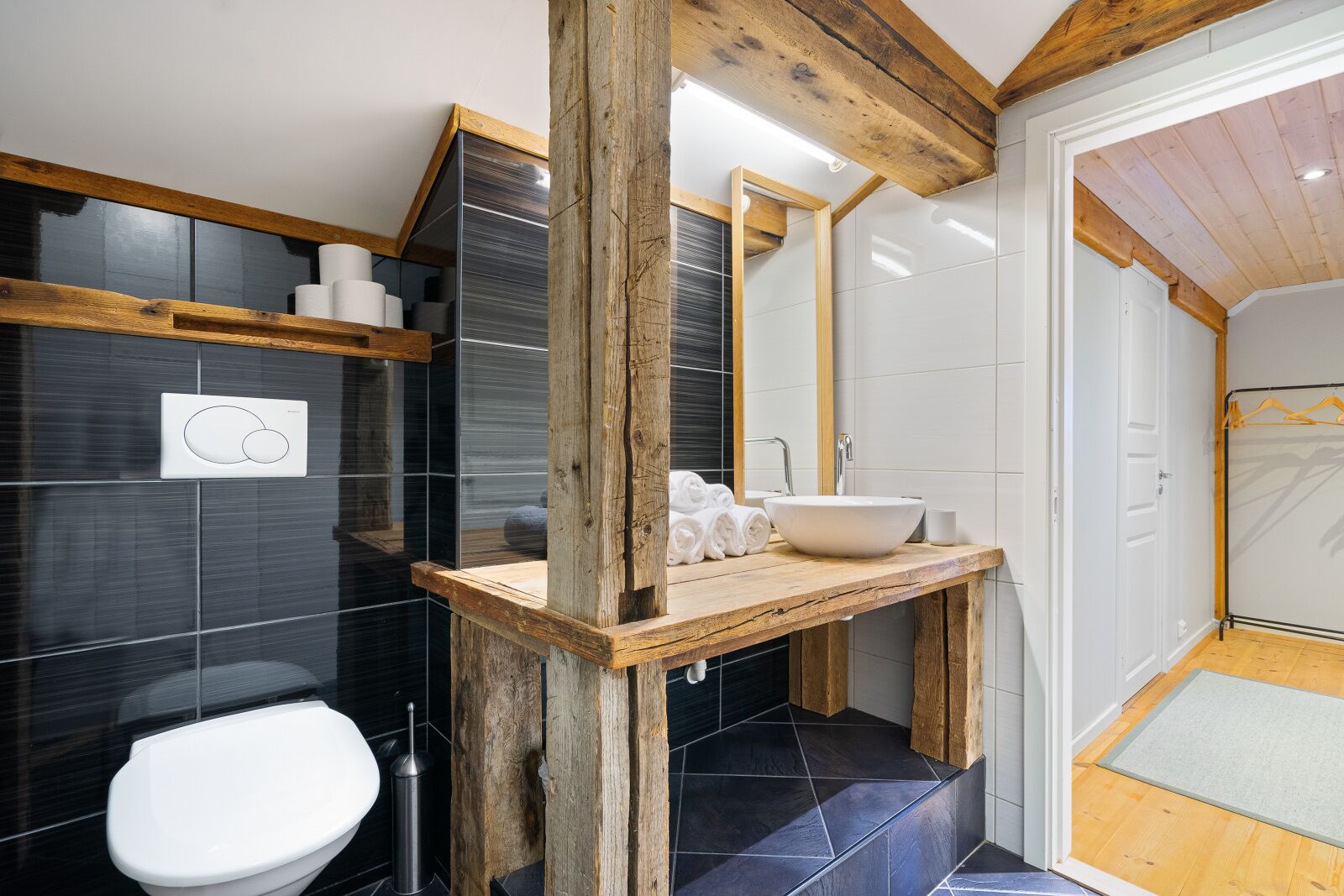 Un baño moderno con tocador de madera, un lavamanos blanco y un espejo grande.
