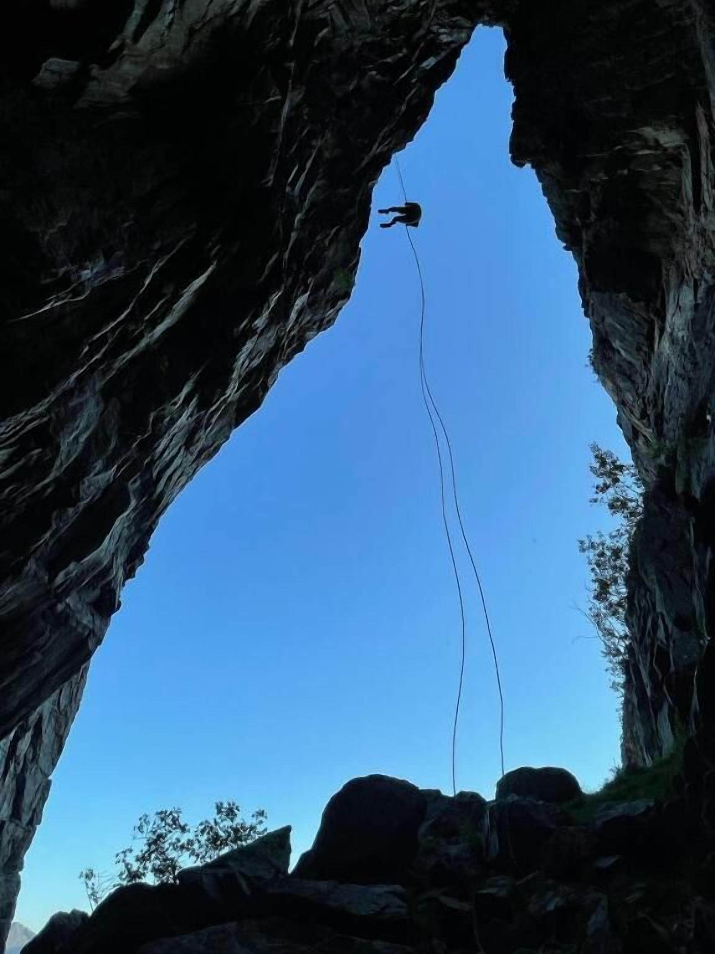 Une personne pratiquant le saut à l’élastique depuis une falaise rocheuse, en passant à travers une arche naturelle.