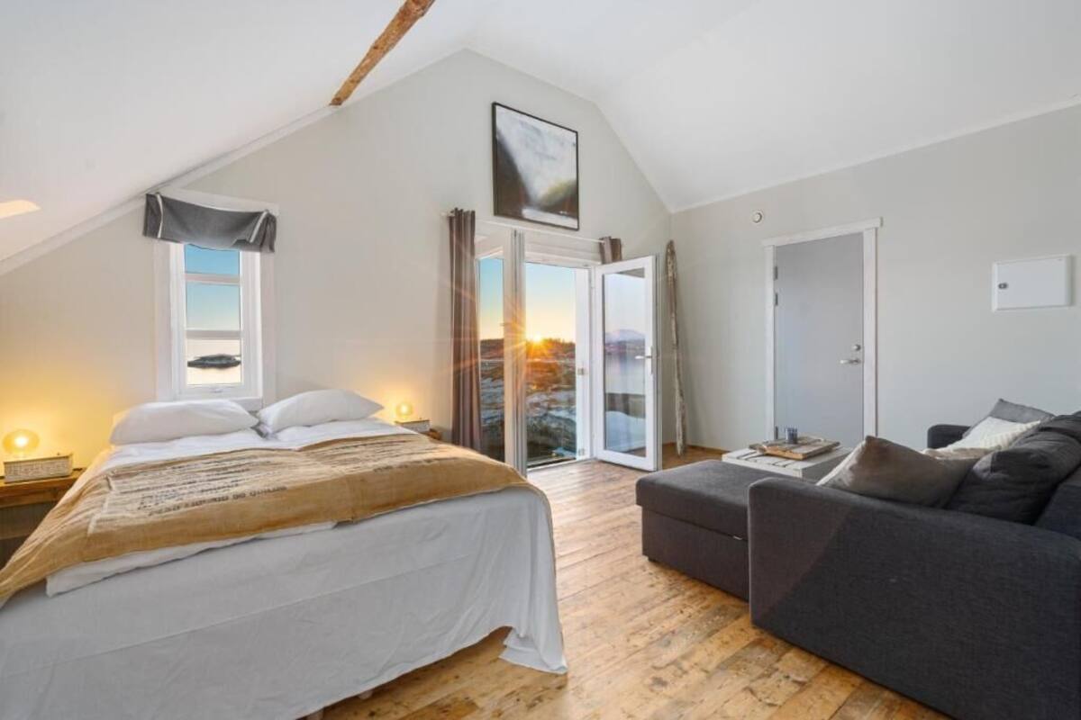 A bedroom with a bed, a sofa, a large window, and a door leading to a balcony.