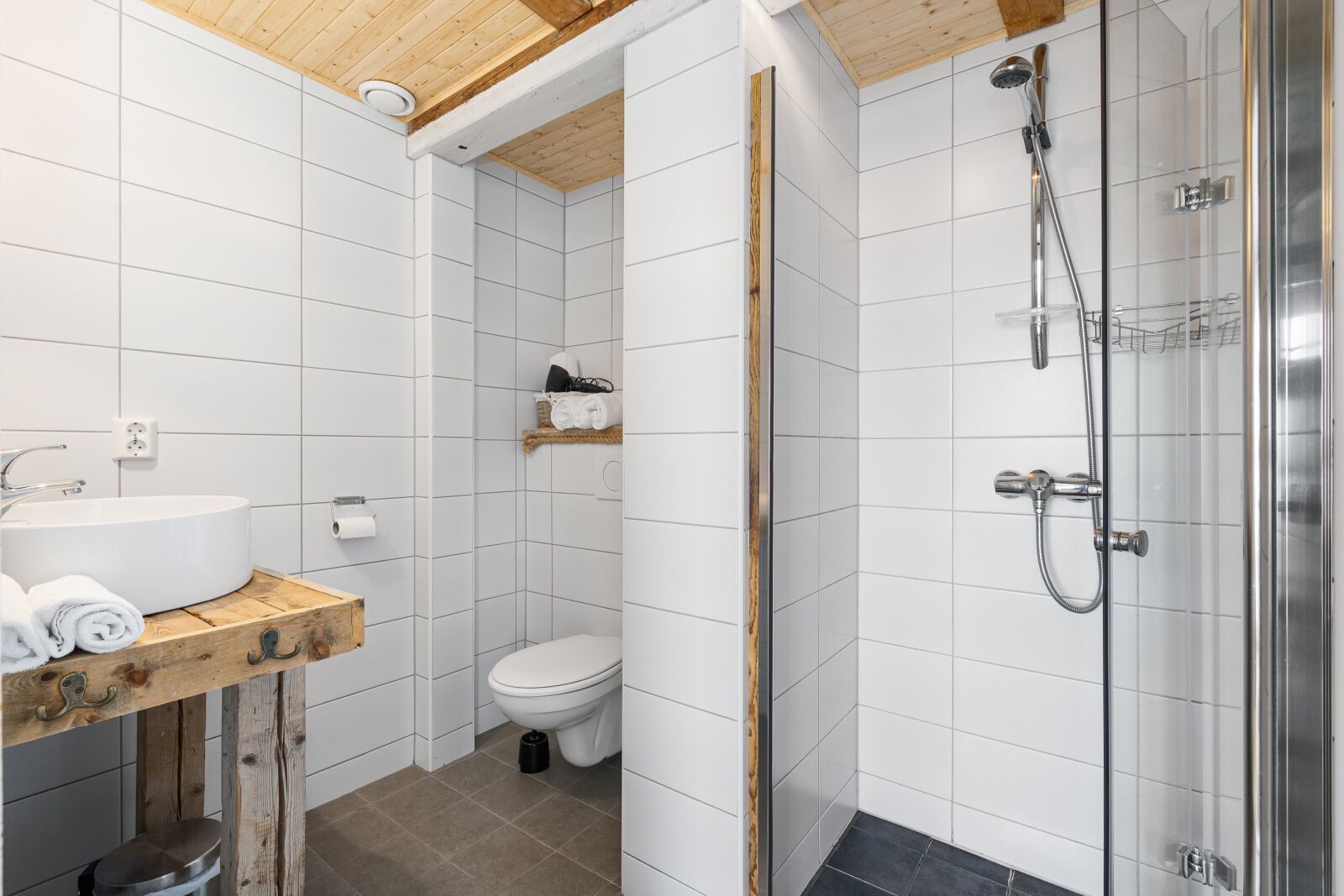 A modern bathroom with a wooden vanity, a toilet, and a glass-enclosed shower area.