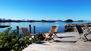A wooden deck with lounge chairs overlooking a calm body of water and a mountainous landscape. - Sveggvika Guesthouse (Averoy)