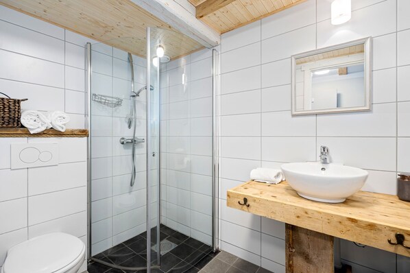 A modern bathroom with a glass-enclosed shower, a wooden vanity with a white sink, and a white toilet. - Sveggvika Guesthouse (Averoy)