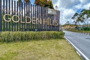 A sign for Golden Hills with a wooden fence and a road in the background. - The Floral Penthouse @ Cameron Highlands (Brinchang)