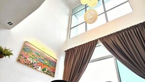 A room with a large window, a painting on the wall, and a ceiling light fixture.