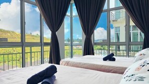 A hotel room with two beds, large windows, and a view of a green landscape.