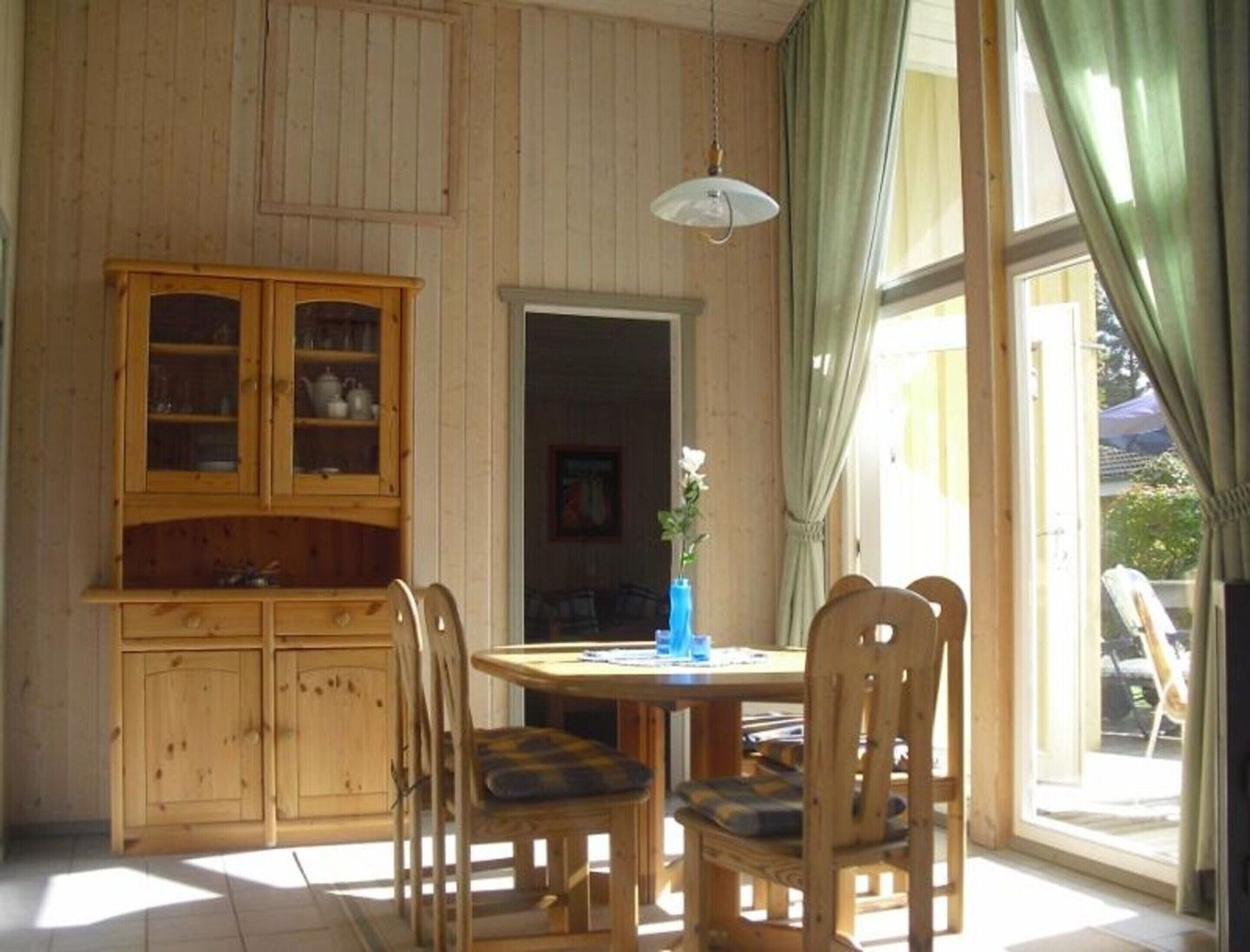 A wooden dining area with a table and chairs, a cabinet with glass doors, and a window with curtains.