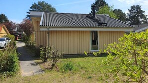 Une maison de plain-pied avec un toit en tuiles, une porte d’entrée et un petit jardin devant.
