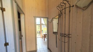 Un couloir étroit aux murs en bois et au sol carrelé, qui mène à un patio ouvert avec une table et des chaises.