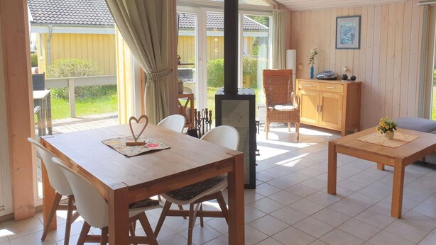 Une pièce chaleureuse avec une table et des chaises en bois, un fauteuil en osier, une armoire et une grande fenêtre avec des rideaux.