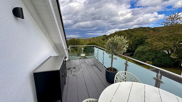 A balcony with a glass railing, a small table, and chairs. - Vacation apartment with lake view in Hattingen - an oasis of well-being in the middle of the Pott! (Hattingen)