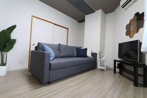 A modern living room with a grey sofa, a flat-screen TV, and a potted plant. - ELLE Namba Villa (Osaka)