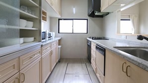 A compact kitchen with light wood cabinets, a microwave, a sink, and a window. - ELLE Namba Villa (Osaka)