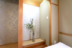 Een kamer met een bed, een houten vloer, een wand met een geometrisch patroon, en een vaas met een plant.