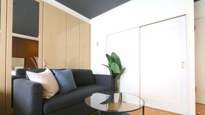 A modern living room with a dark grey sofa, a glass coffee table, and a potted plant. - ELLE Namba Villa (Osaka)