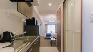 A narrow hallway leading to a bedroom with a bed, a small table, and a window. - leopard Shinsaibashi (Osaka)