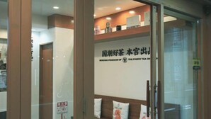 A reception area with a sign indicating a tea shop. There is a wooden bench with cushions, a fire extinguisher, and a glass door. - leopard Shinsaibashi (Osaka)