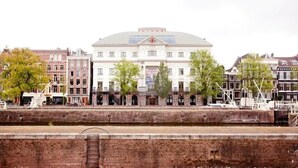 Un edificio histórico con una cúpula central, flanqueado por arquitectura europea tradicional, ubicado junto a un canal.