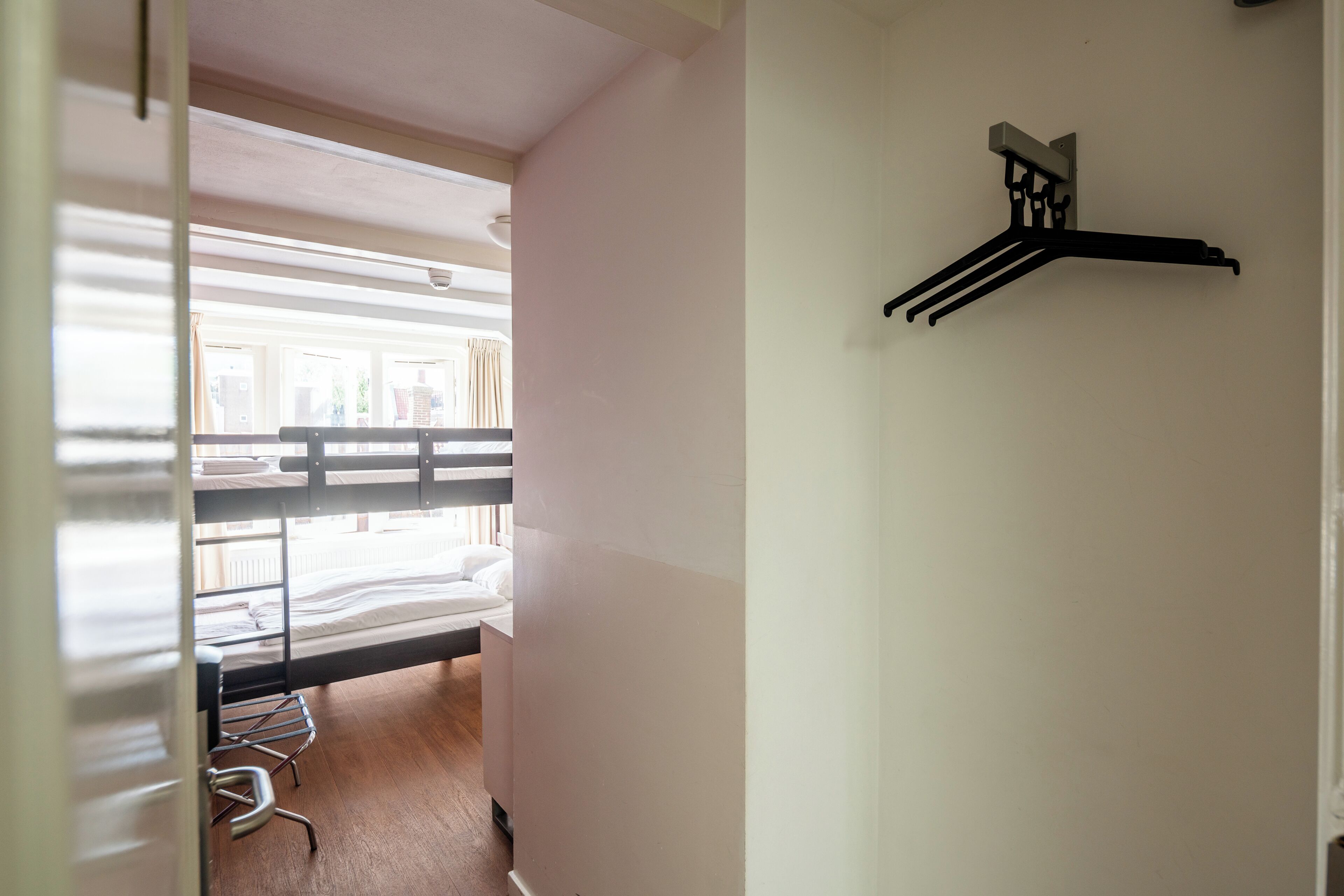 A room with bunk beds, a hanging clothes rack, and a door leading to another room.