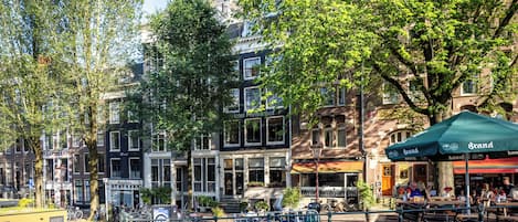 A riverside view of a historic building with a restaurant patio and bicycles.