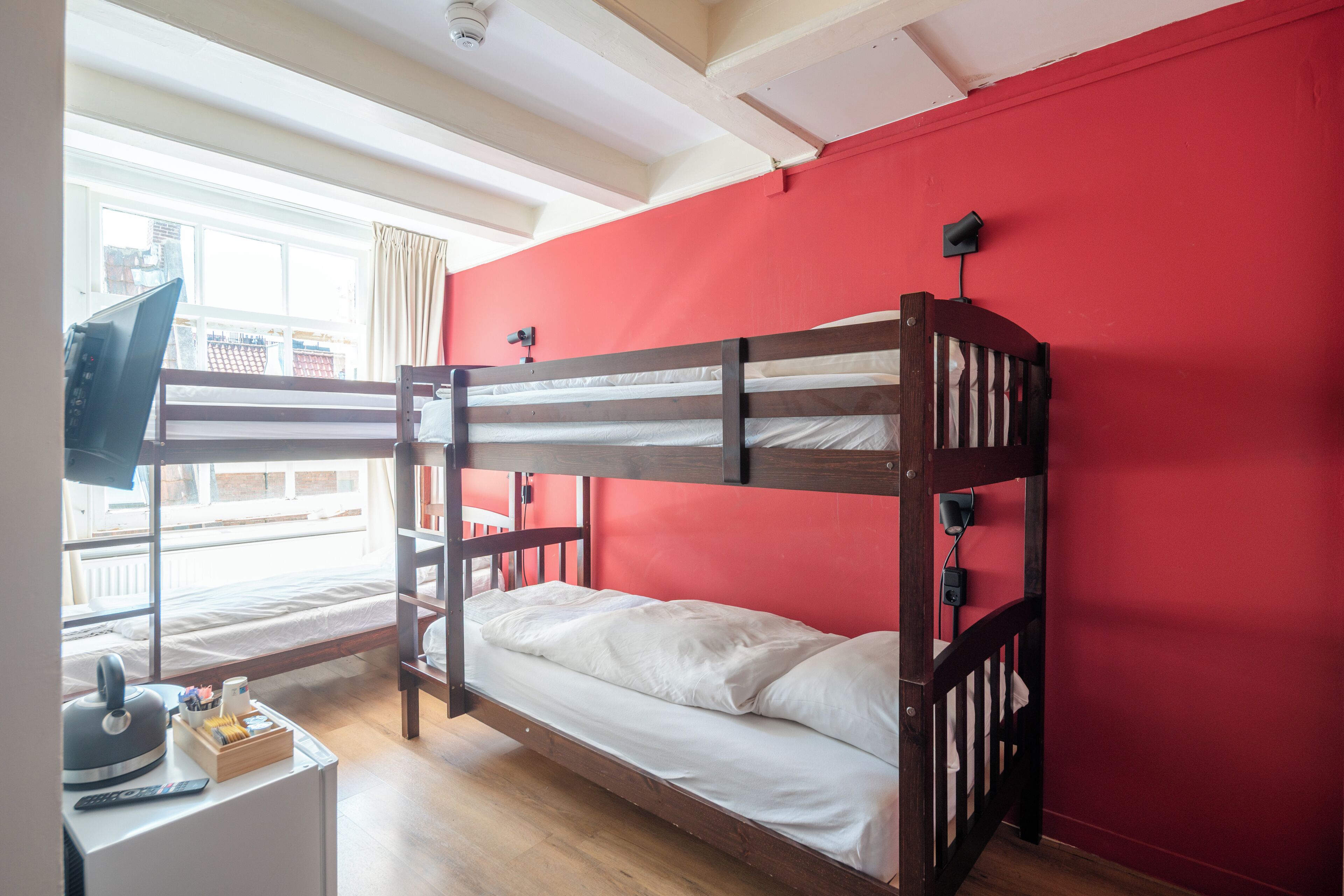 Une chambre avec un lit superposé, une télévision, un bureau en bois et une fenêtre donnant sur des immeubles.