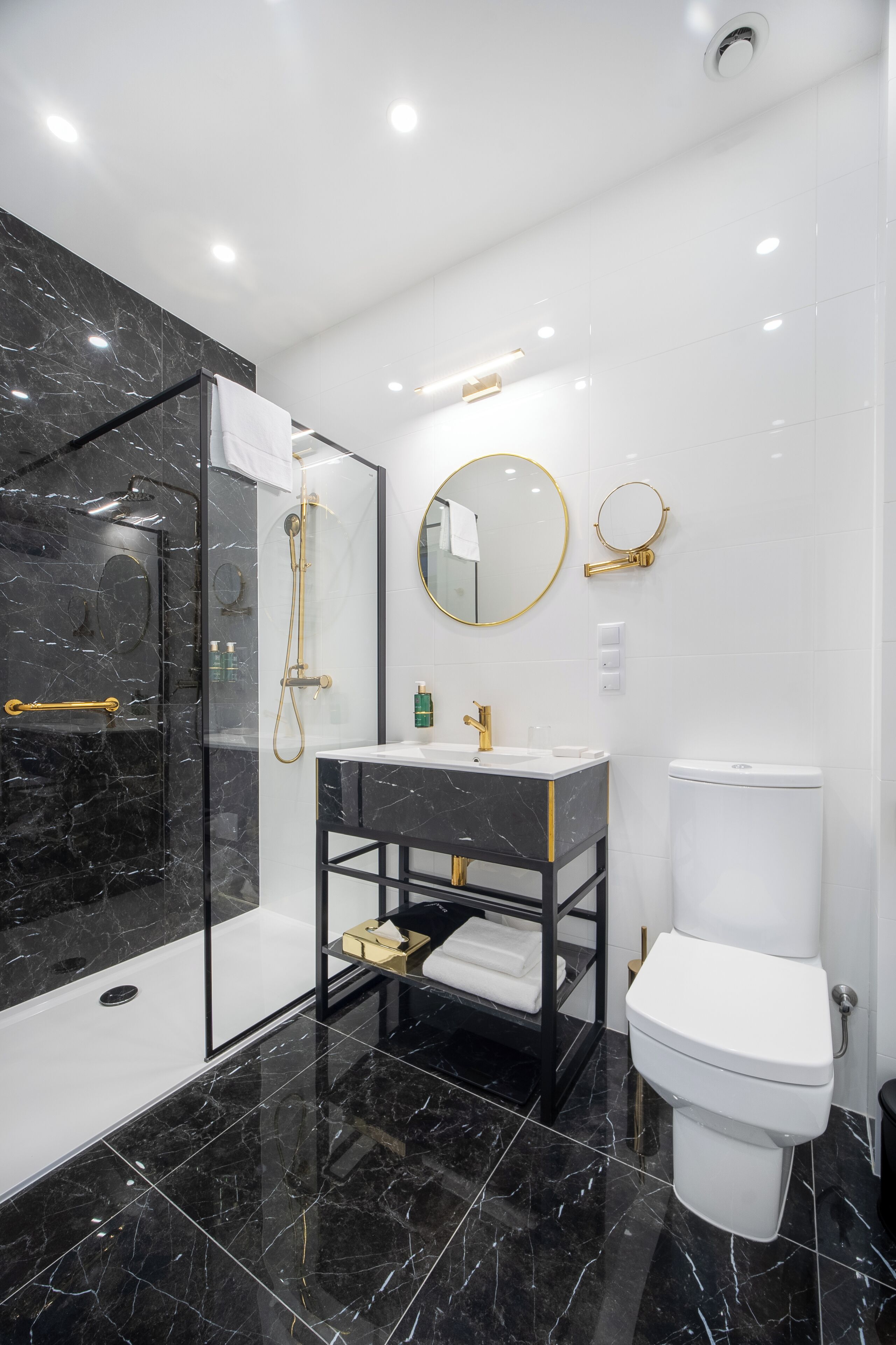 Ein modernes Badezimmer mit einer Duschkabine, einem Waschtisch mit Goldarmatur und einer Toilette.