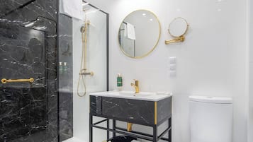 Ein modernes Badezimmer mit einer Duschkabine, einem Waschtisch mit Goldarmatur und einer Toilette.