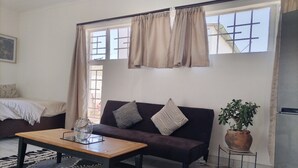 Ett vardagsrum med en soffa, ett soffbord, en matta, en krukväxt och ett fönster med gardiner.