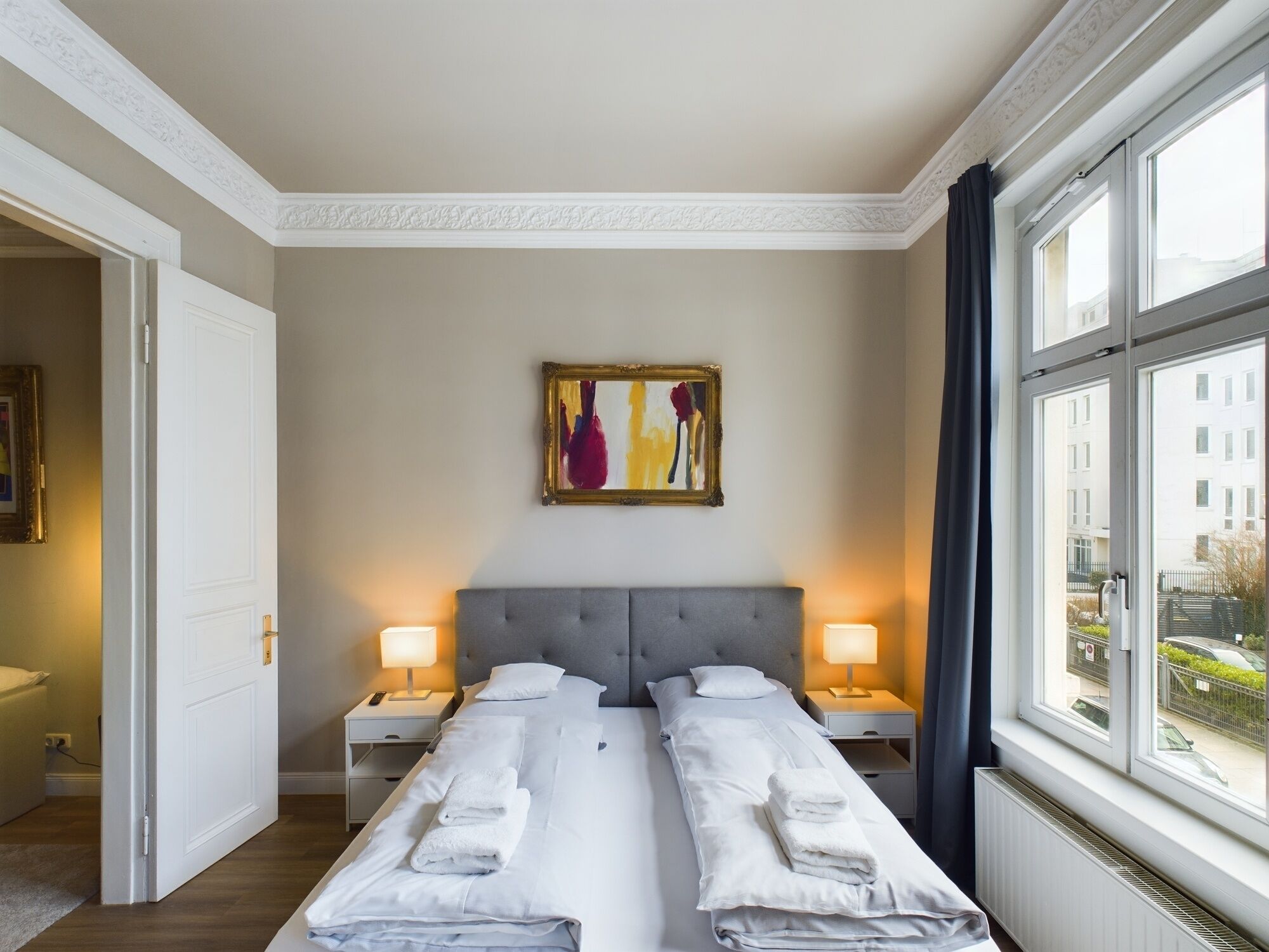 Ein Hotelzimmer mit einem Doppelbett, zwei Nachttischen mit Lampen, einem Bild an der Wand und einem Fenster mit Blick nach draußen.