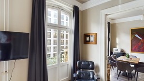 A modern hotel room with a large window, a black leather chair, a dining area with a table and chairs, and a flat-screen TV mounted on the wall. - Art Apartments (Hamburg)