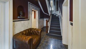 A grand staircase with a marble floor and a leather sofa in a hallway with dark walls and a ceiling light. - Art Apartments (Hamburg)