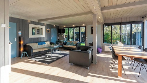 Un espacio habitable amplio con techo de madera, un sofá, una mesa baja y una mesa de comedor con sillas.