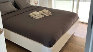 Een moderne slaapkamer met een groot bed, een nachtkastje en een raam met jaloezieën.