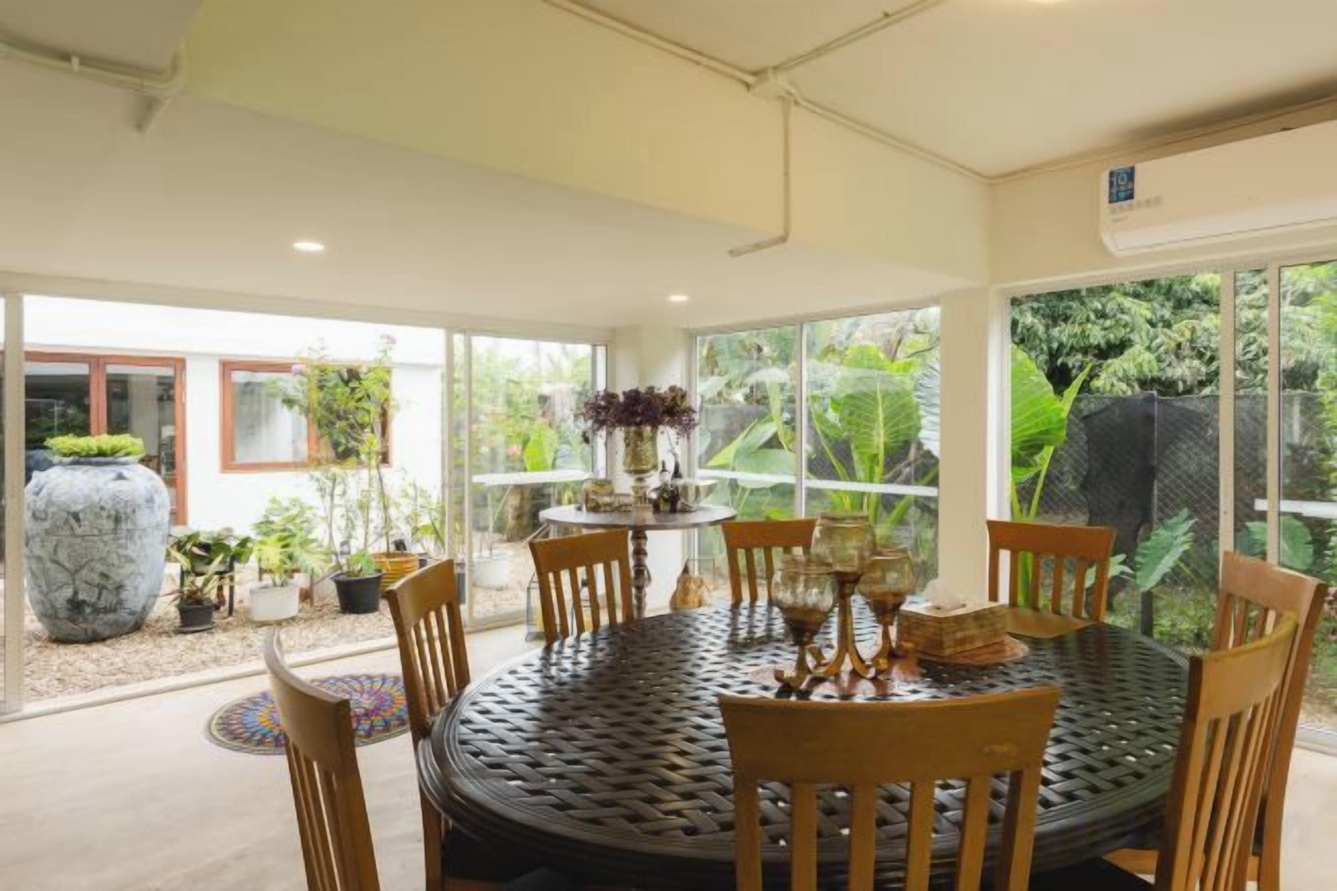 A round dining table with chairs, surrounded by potted plants and a large vase.