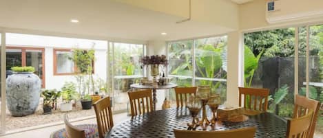 A round dining table with chairs, surrounded by potted plants and a large vase.