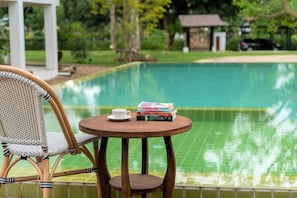 Escena junto a la piscina con una silla, una mesa y un libro.