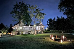 A large, multi-story house with a well-maintained lawn and a series of lit fires.