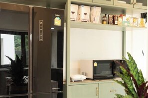 Una kitchenette con refrigerador, microondas y estantes con productos envasados.
