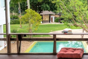 Vista desde una habitación con piscina, una terraza de madera y un edificio pequeño al fondo.