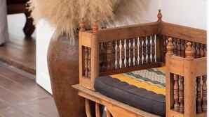 A wooden chair with a cushioned seat and backrest, positioned next to a white wall and a large potted plant. - Phi Private Villa: Luxury 4 beds Riverside & Pool: Near old townBreakfast, Laundry, Free pickup (Chiang Mai)
