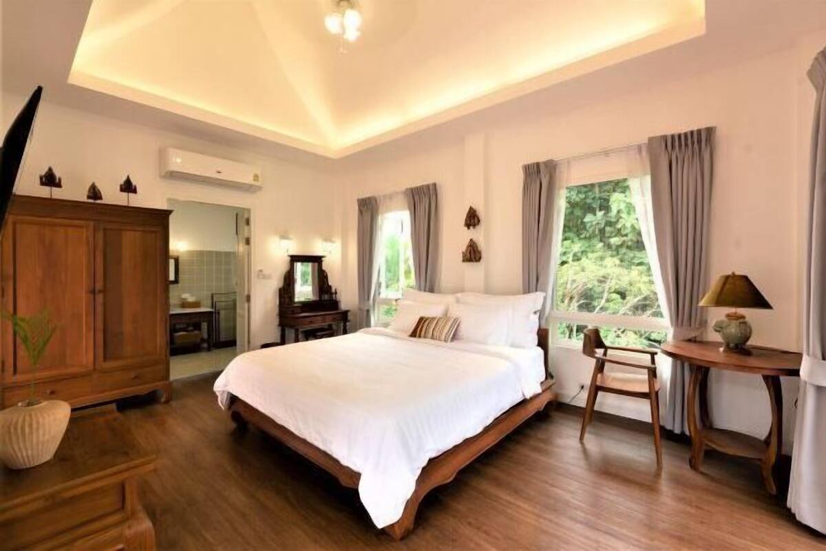 A spacious bedroom with a large bed, wooden furniture, and a view of greenery outside.