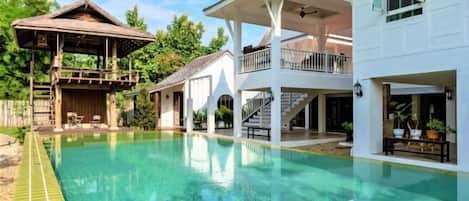 Uma piscina grande com deck de madeira e um gazebo, cercada por edifícios brancos com varandas e áreas de estar ao ar livre.